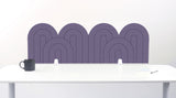 A purple felt desk divider with a wavy, layered arch pattern, shown standing behind a white desk with a black mug on the left and a notepad on the right.
