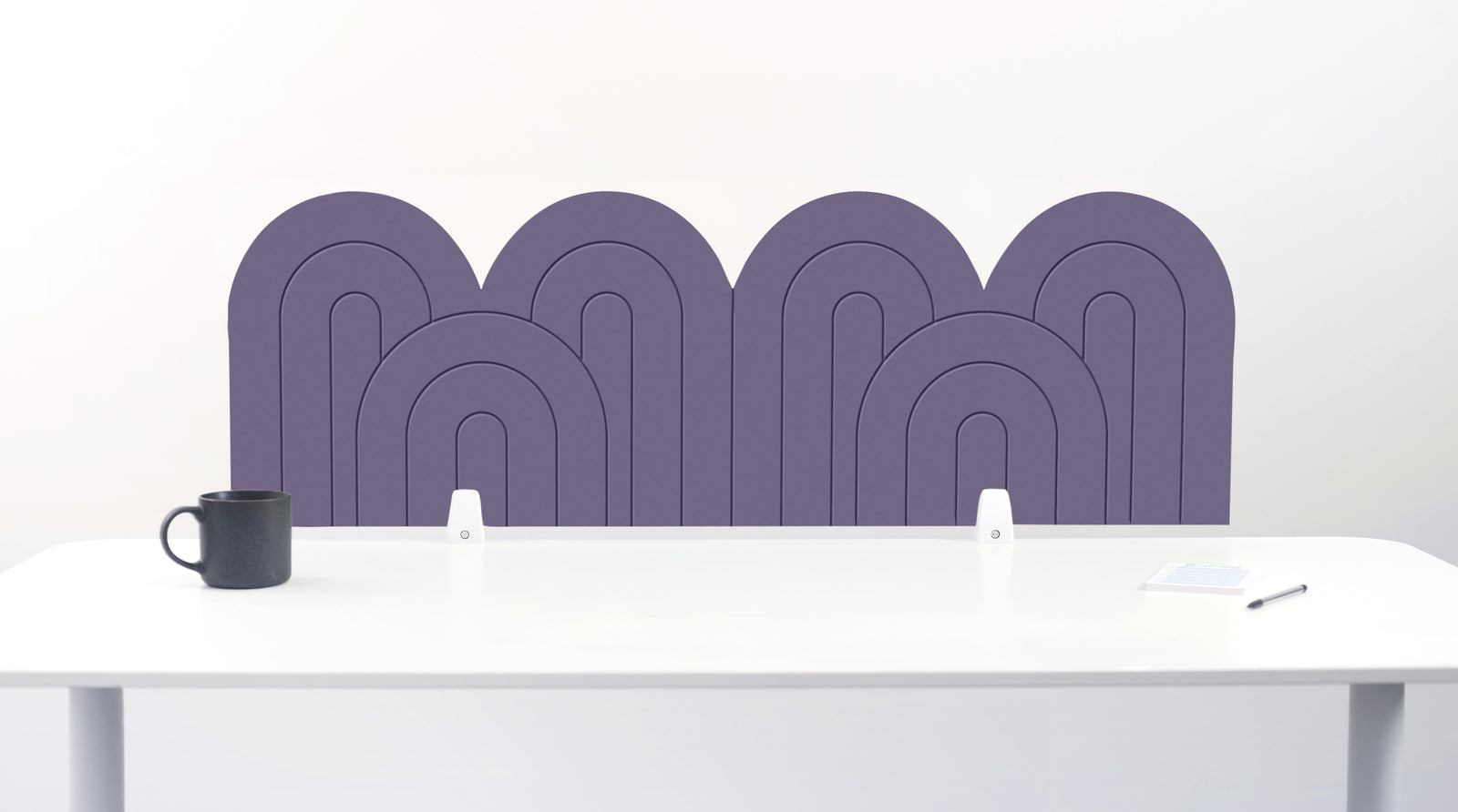 A purple felt desk divider with a wavy, layered arch pattern, shown standing behind a white desk with a black mug on the left and a notepad on the right.
