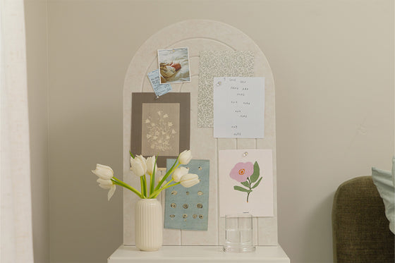 Decorative wall board with a vase of flowers, framed pictures, and notes on a neutral background