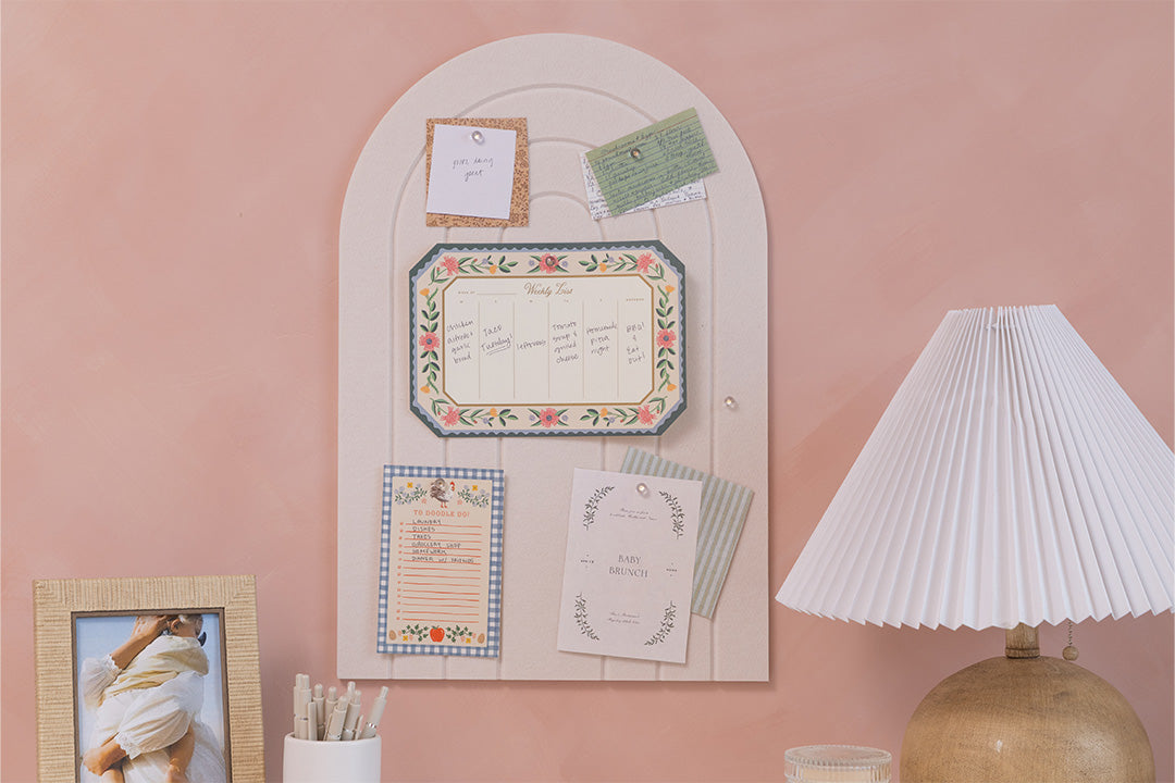 Decorative wall panel with framed pictures and notes on a pink wall, next to a lamp.