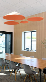 Four rust-orange circular acoustic baffles suspended from ceiling above conference table in modern office space.