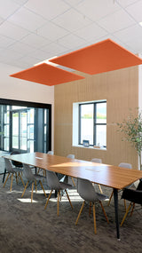 Two rust-orange square flat acoustic baffles suspended from ceiling above conference table in office space.