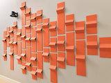 Three-dimensional orange tiles with varied depths arranged on a white wall in an abstract pattern.