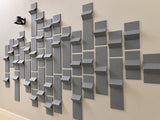 Three-dimensional gray tiles arranged in a geometric pattern on a beige wall, creating depth and shadow variation.