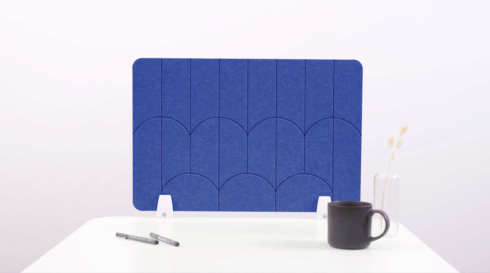 A blue colored felt desk divider with a scalloped design of lines and arches. 