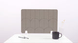 A brown colored felt desk divider with a scalloped design of lines and arches. 