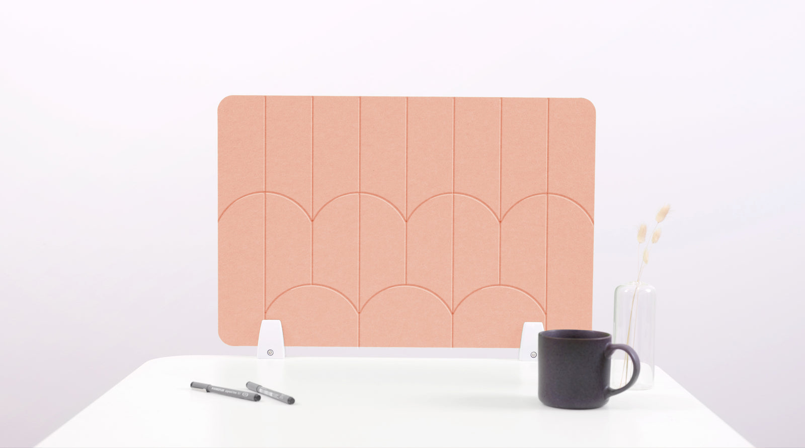 A peach colored felt desk divider with a scalloped design of lines and arches.