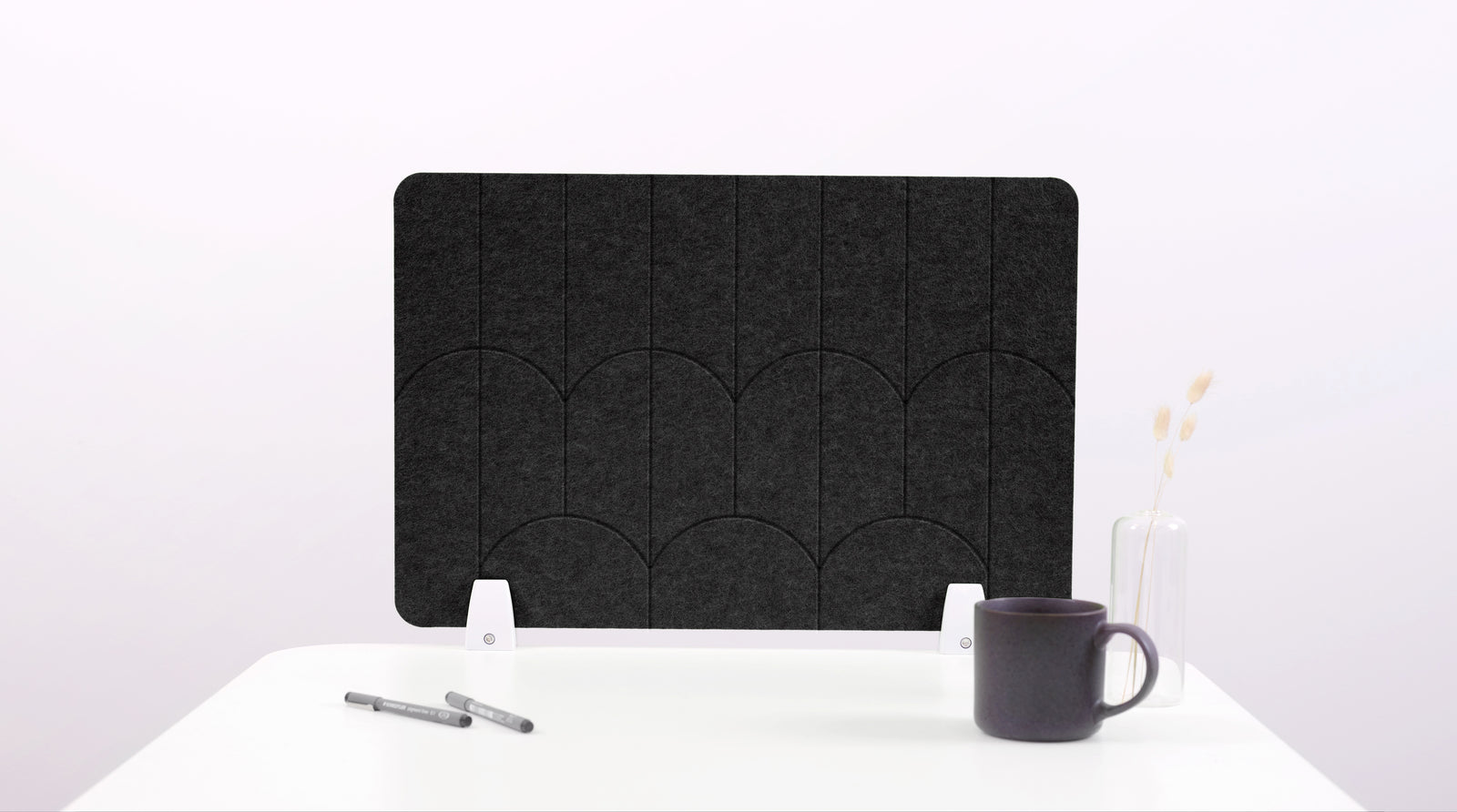 A black felt desk divider with a scalloped design of lines and arches. 