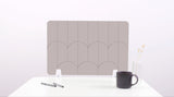 A tan colored felt desk divider with a scalloped design of lines and arches. 