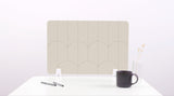 A light tan colored felt desk divider with a scalloped design of lines and arches. 