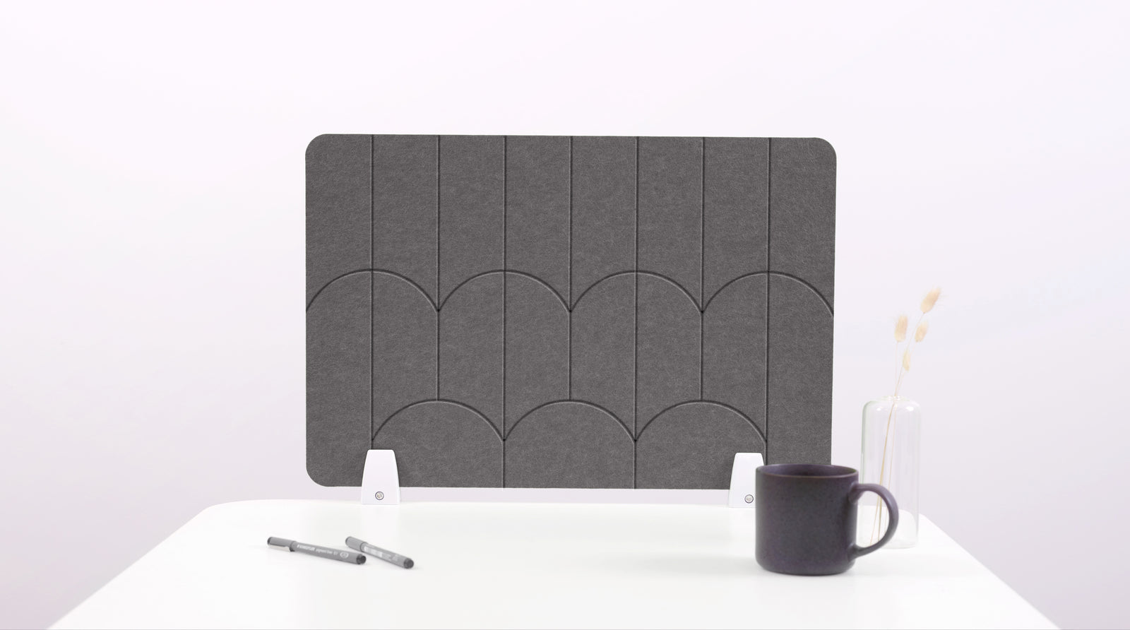 A dark gray felt desk divider with a scalloped design of lines and arches. 