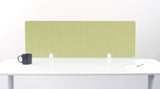 A light sage green felt desk divider with a scalloped wave pattern, mounted on a white desk with a black mug on the left and a small notepad on the right.