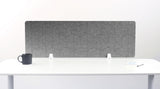 A light gray felt desk divider with a scalloped wave pattern, mounted on a white desk with a black mug on the left and a small notepad on the right.