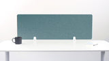 A teal blue felt desk divider with a scalloped wave pattern, mounted on a white desk with a black mug on the left and a small notepad on the right.