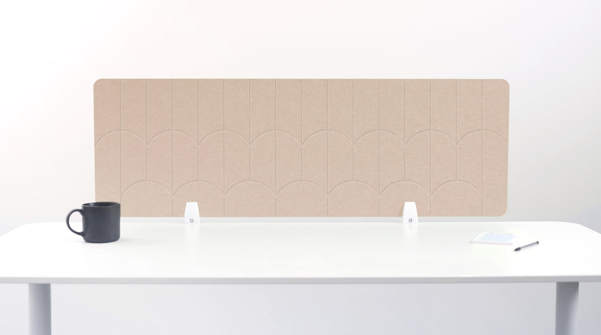 A tan felt desk divider with a scalloped wave pattern, mounted on a white desk with a black mug on the left and a small notepad on the right.