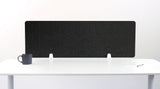 A dark gray felt desk divider with a scalloped wave pattern, mounted on a white desk with a black mug on the left and a small notepad on the right.