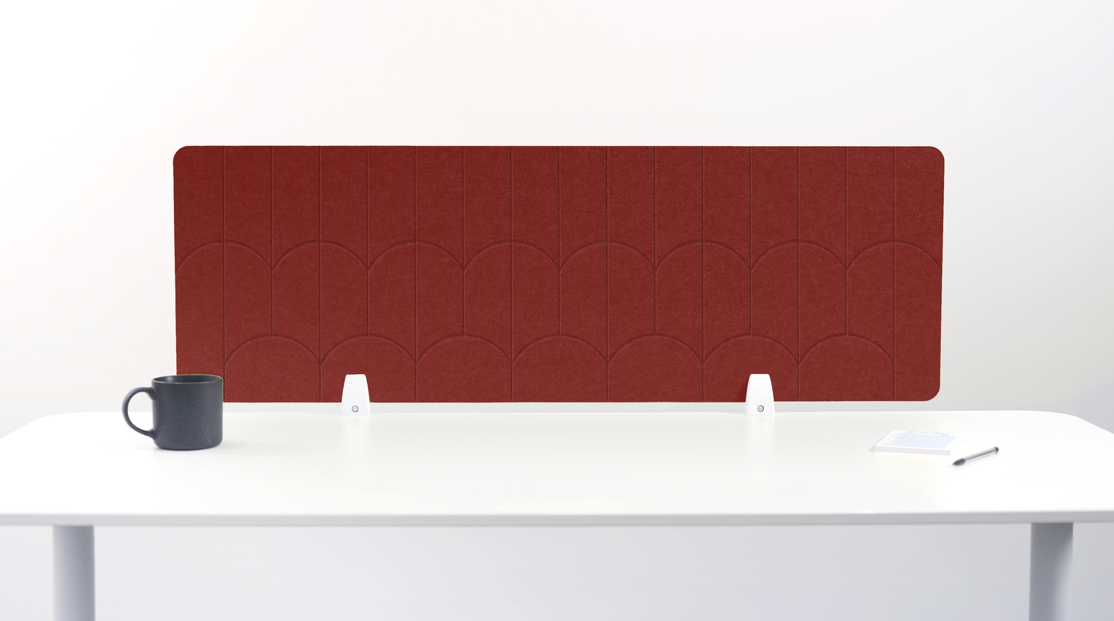 A red felt desk divider with a scalloped wave pattern, mounted on a white desk with a black mug on the left and a small notepad on the right.