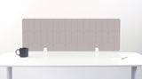 A tan felt desk divider with a scalloped wave pattern, mounted on a white desk with a black mug on the left and a small notepad on the right.