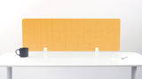 A mustard yellow felt desk divider with a scalloped wave pattern, mounted on a white desk with a black mug on the left and a small notepad on the right.