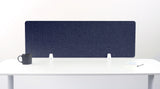 A navy blue felt desk divider with a scalloped wave pattern, mounted on a white desk with a black mug on the left and a small notepad on the right.