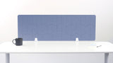 A blue fabric desk divider with a scalloped wave pattern, mounted on a white desk with a black mug on the left and a small notepad on the right.