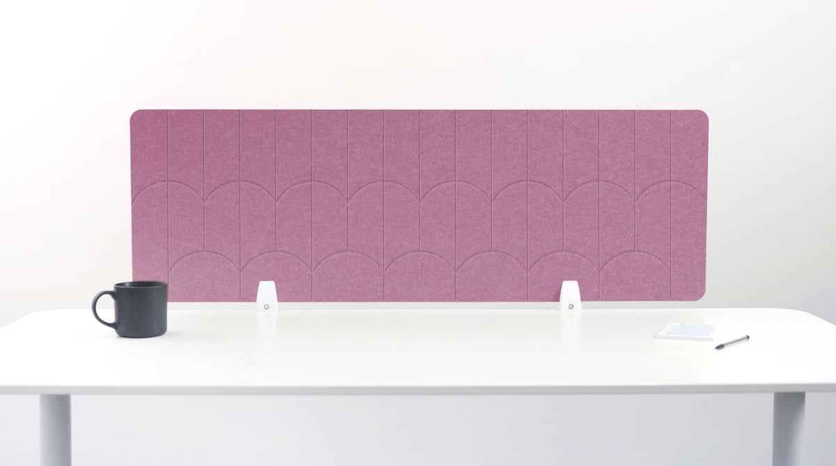 A rectangular pink felt desk divider with a scalloped pattern, mounted on a white desk with a black mug on the left and a small notepad on the right.