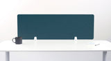 A slate blue felt desk divider with a scalloped wave pattern, mounted on a white desk with a black mug on the left and a small notepad on the right.