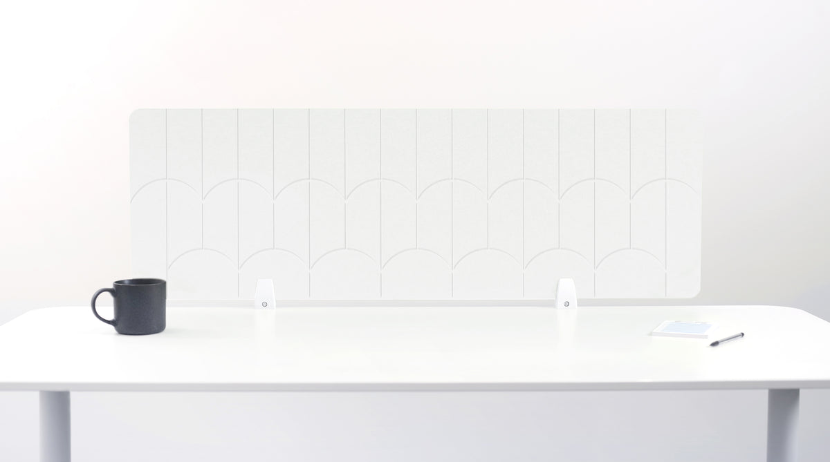 A white felt desk divider with a scalloped wave pattern, mounted on a white desk with a black mug on the left and a small notepad on the right.