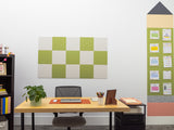 Green and cream checkered pinboard mounted on white wall above wooden desk.
