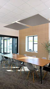 Two overlapping dark gray square acoustic panels suspended from white drop ceiling above conference table.