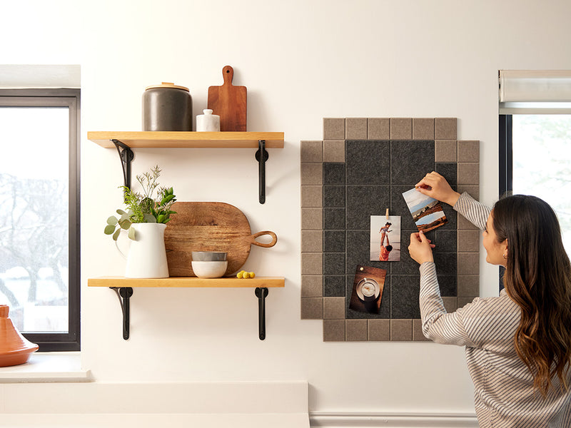 A Felt Right wall art design in shades of brown that is pinnable next to two shelves. Woman pinning photos onto the felt tiles