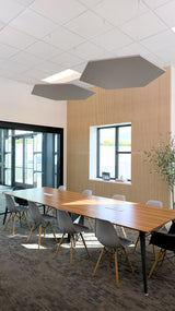 Two gray hexagon-shaped acoustic baffles suspended from ceiling in modern conference room setting.