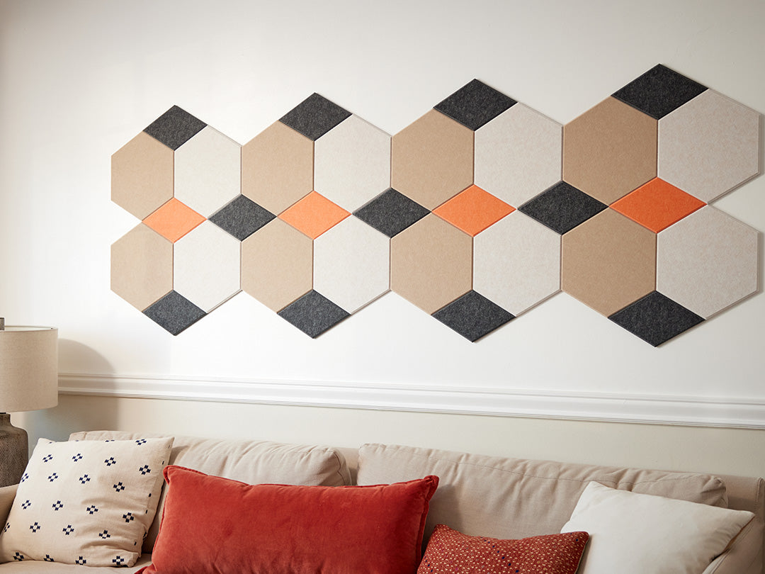 A Felt Right wall art design in shade of cream, orange, and black on light colored wall above a couch in a living room