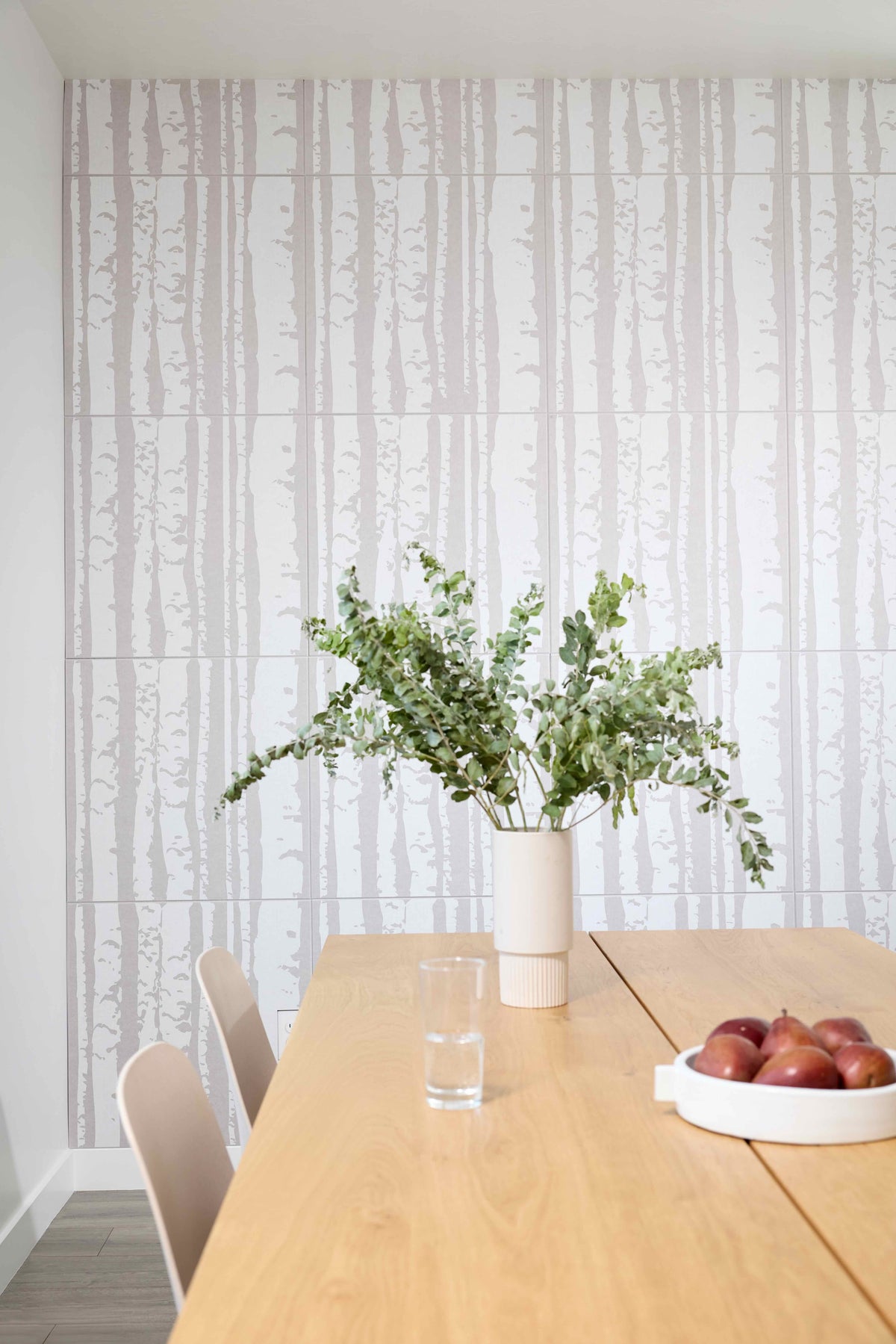 Dining room with a wooden table, vase of flowers, and apples against a patterned wall.
