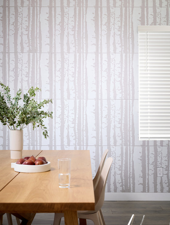 Dining room with a wooden table, glass, apples, and a vase against a patterned wall.