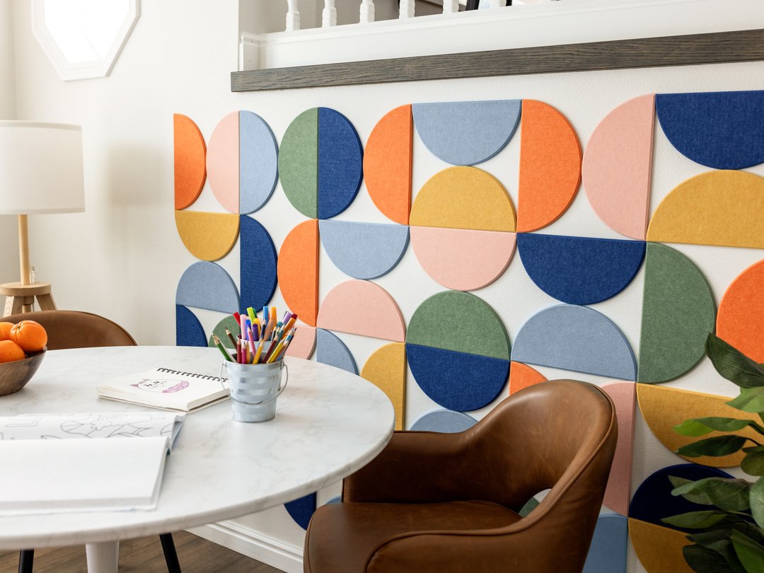 Felt right wall art design by a kitchen table in shades of pink, blue, green, and orange felt half circle tiles with some art supplies on the table.