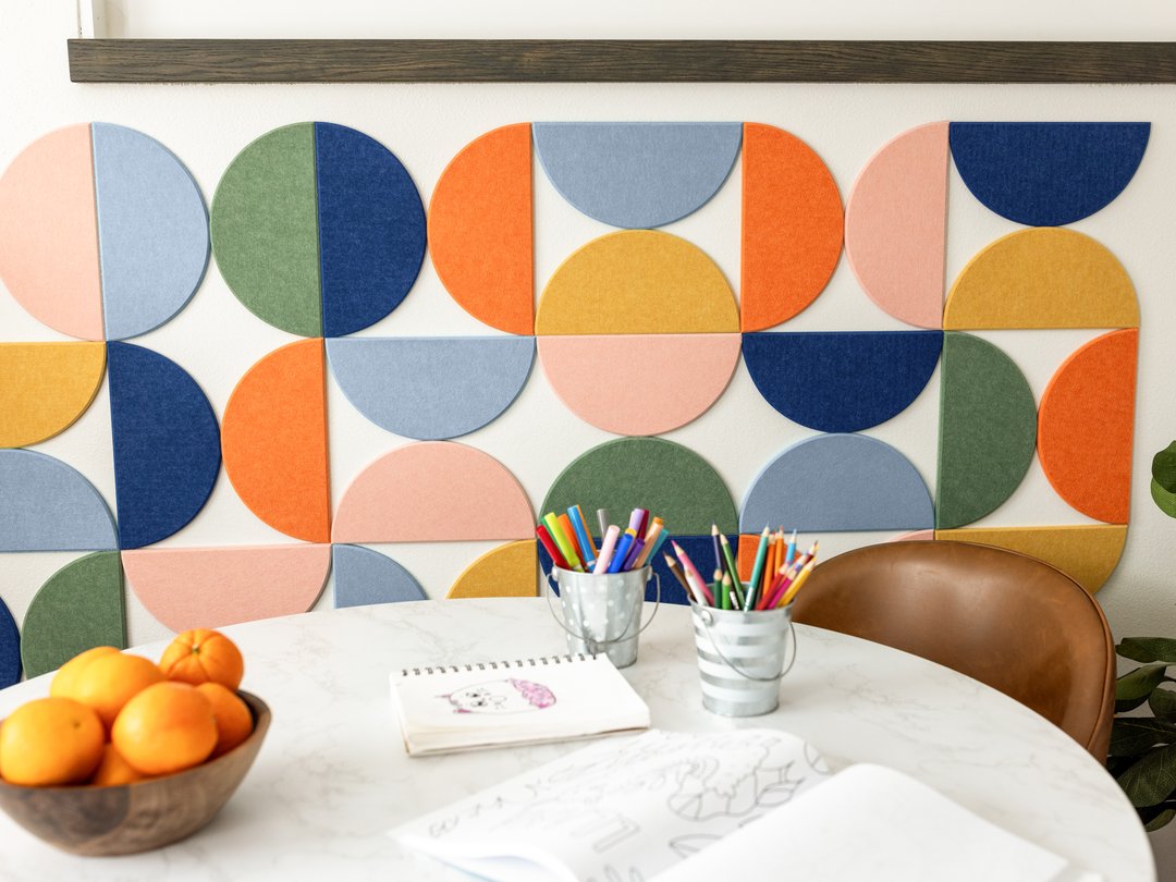 Felt right wall art design by a kitchen table in shades of pink, blue, green, and orange felt half circle tiles with some art supplies on the table.