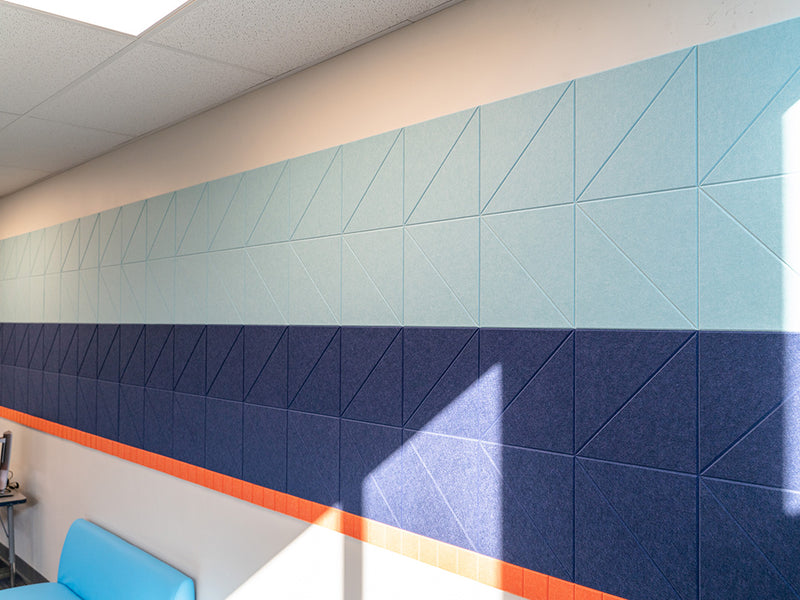 A Felt Right wall art design in shades of blue and orange felt tiles creating a strip along a white wall in a classroom setting.