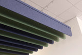 Layered acoustic ceiling panels in blue and green hanging in a staggered pattern under a white ceiling tile.