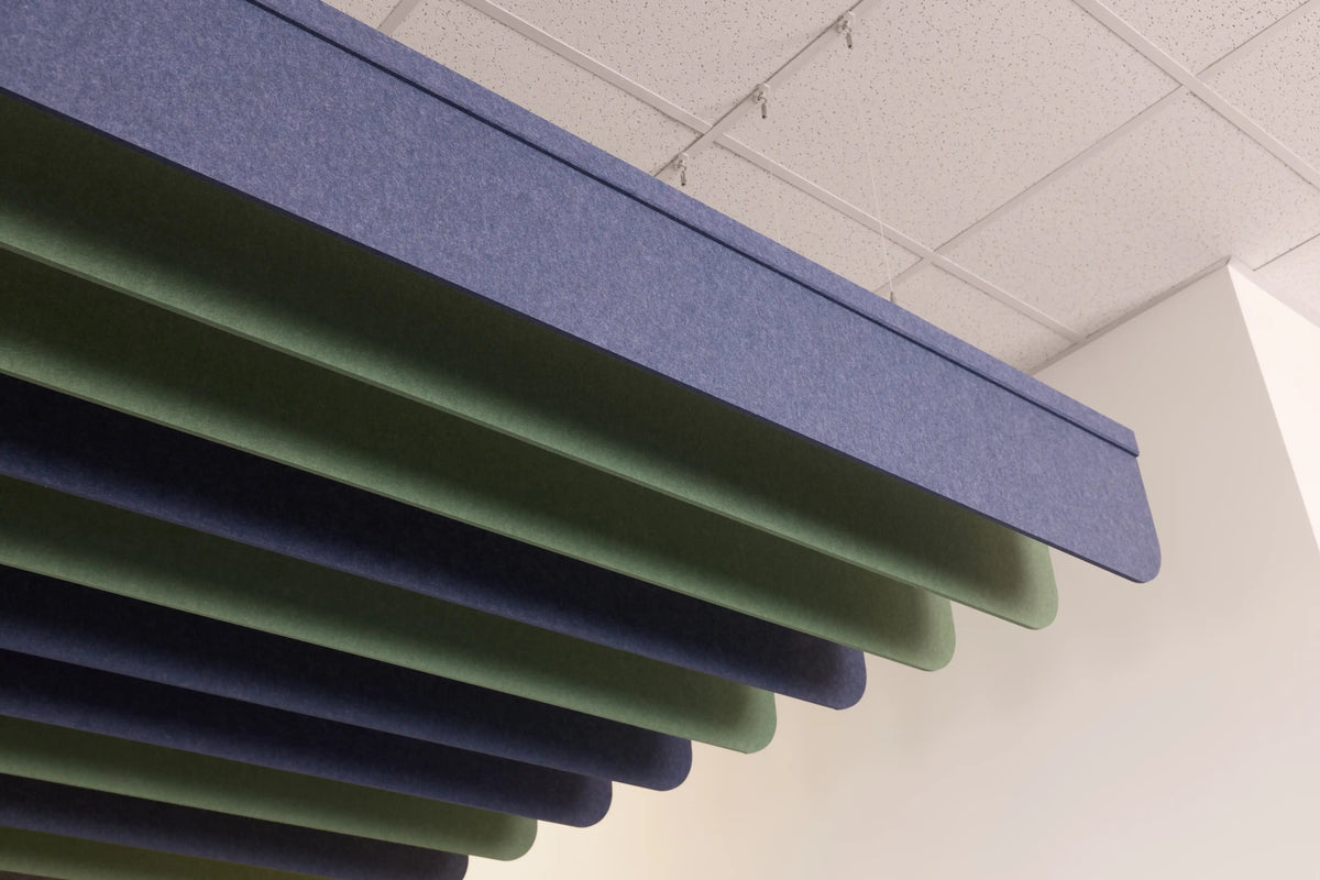 Layered acoustic ceiling panels in blue and green hanging in a staggered pattern under a white ceiling tile.