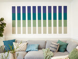 Eleven vertical color blocks in navy, teal, sage green, and beige arranged in horizontal rows on white wall above gray sofa.
