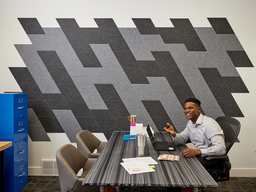 The Felt Right wall art design in shades of grey and black creating a slanted look in an office with a desk in the center and a filing cabinet on the side and a man working on his laptop