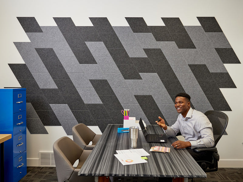The Felt Right wall art design in shades of grey and black creating a slanted look in an office with a desk in the center and a filing cabinet on the side and a man working on his laptop