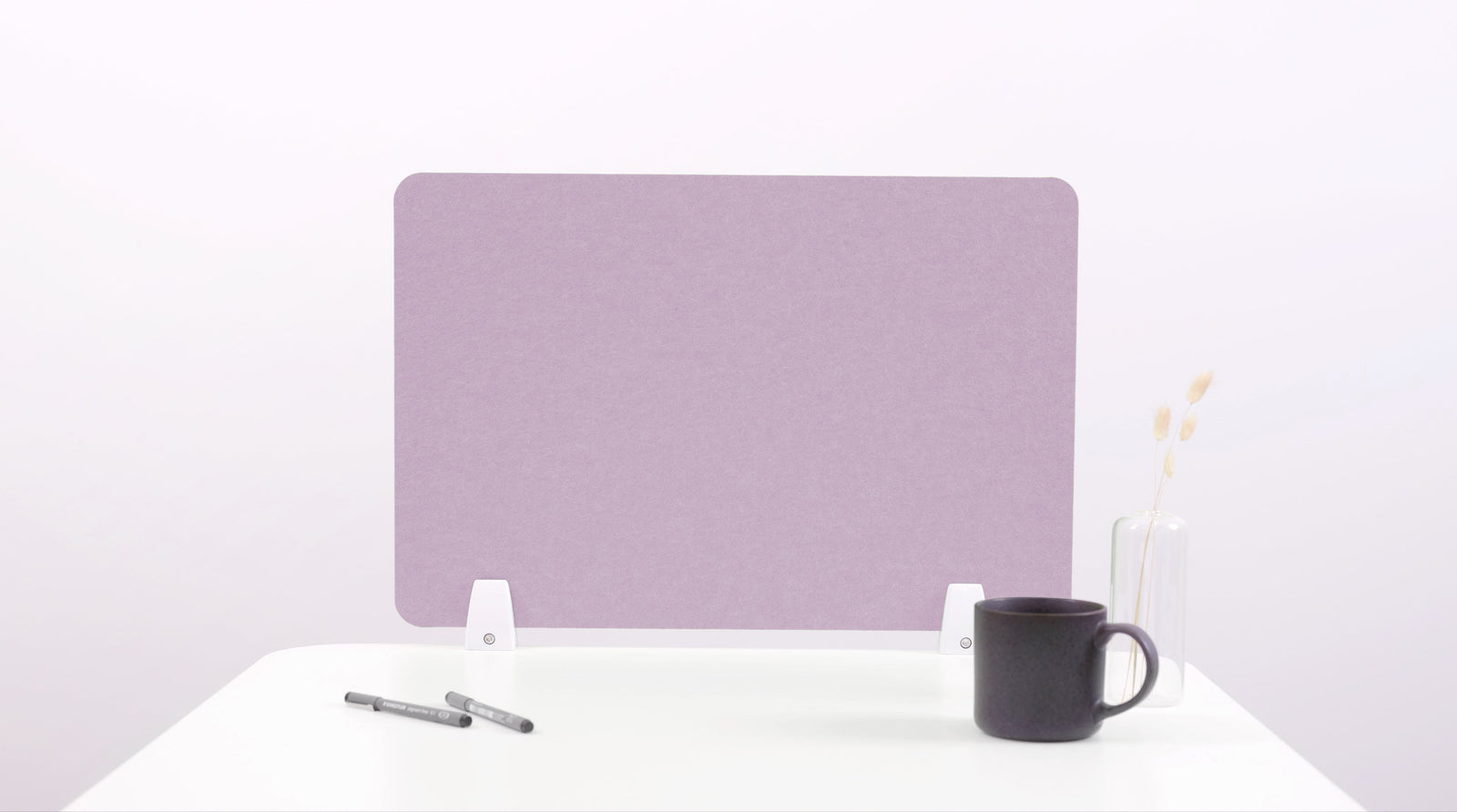 A lilac-colored felt desk divider placed on a desk with a pen and a mug on its surface.