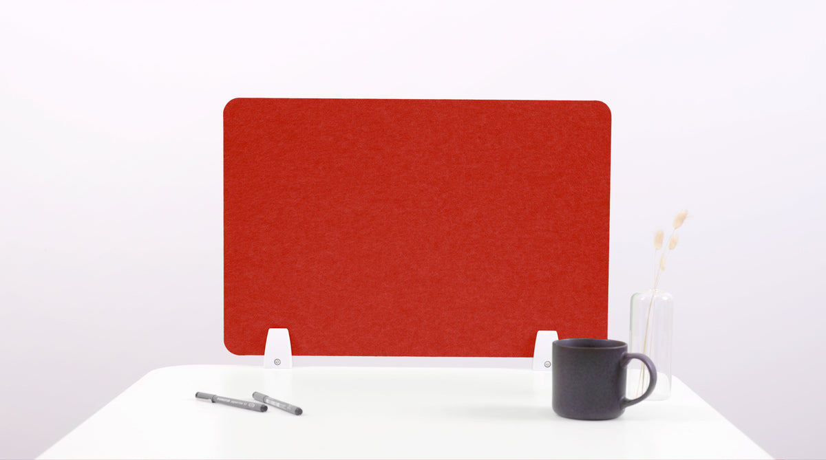 A red felt desk divider placed on a white desk, with a black pen and a cup on its surface.