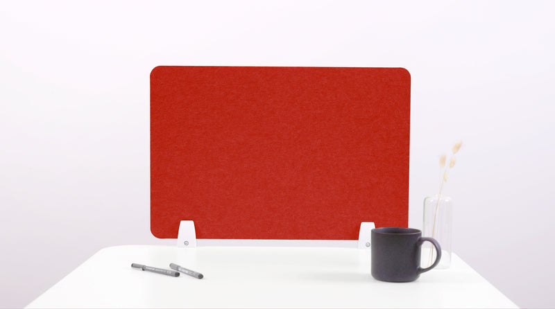 A red felt desk divider placed on a white desk, with a black pen and a cup on its surface.