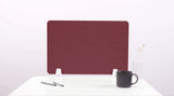 Burgundy desk divider with rounded corners mounted on white desk next to coffee mug and pens.