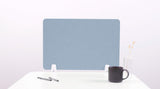 Blue desk divider with white mounting brackets on white surface, flanked by pens, mug, and vase.