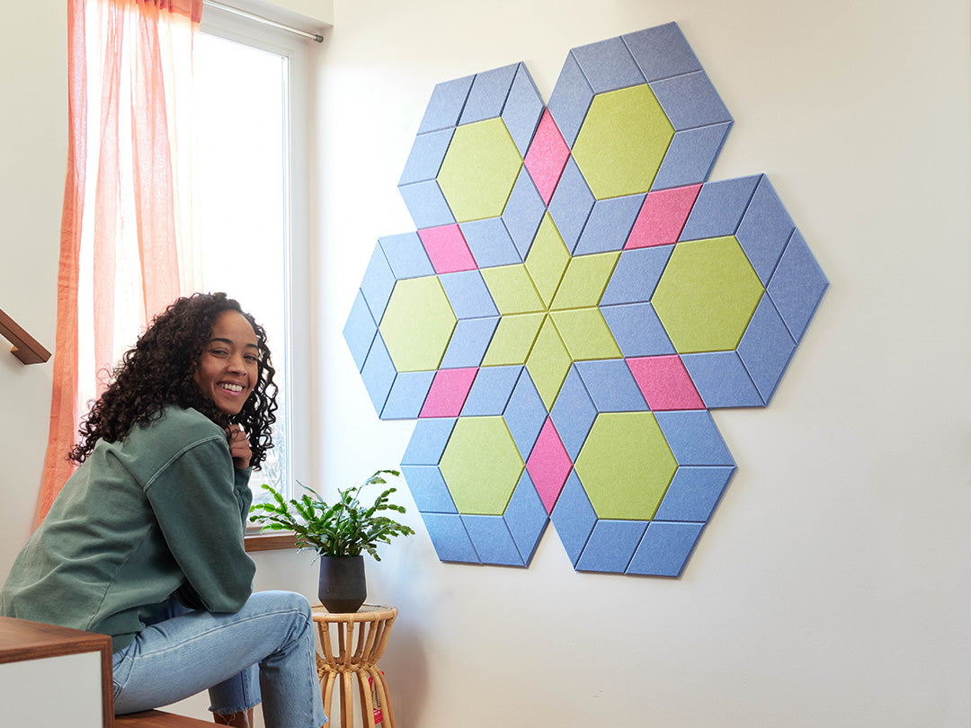Woman sitting next to colorful geometric wall panels in a room with a window and plant.