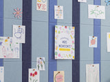 Blue and navy pinstriped bulletin board with various papers and drawings pinned to surface.